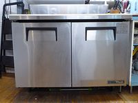 Front view of closed unit showing stainless steel doors, handles, True logo and casters.