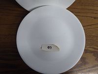 Close-up of single white Corelle dining plate showing the flat surface and slight rim with label '97'.
