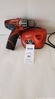 Milwaukee cordless hand drill and red charger side view on white background.