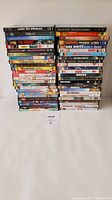 Photo showing two stacked columns of 25 DVDs each in their cases, with visible titles and colorful DVD cover art.