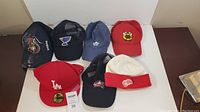 Seven sports caps displayed on flat surface showing various NHL teams' logos and styles.