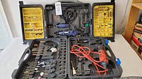 Lot of rotary tools and two carrying cases with yellow trays of accessories, tools, and attachments organized inside