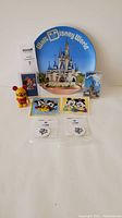 Photo showing lot items arranged: Disney World plate with Cinderella Castle, two decks of Disney cards, two Mickey and Minnie patches, two Disney pogs, yellow Mickey Mouse figurine