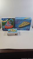 Photo of three boxed new inflatables: pizza float, sprinkler toy, and colorful ring