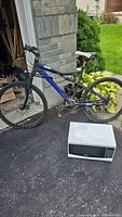 Full side view of blue and black Reebok Oregon mountain bike next to a microwave. The bike frame size is 19 inches for adults.