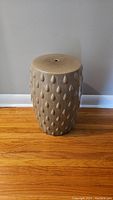Front view of the light brown ceramic garden stool with raised teardrop shapes on the body.