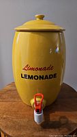 Full front view of yellow ceramic lemonade dispenser with lid and printed text