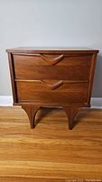 Front view of mid century side table showing two drawers with carved handles and tapered legs.