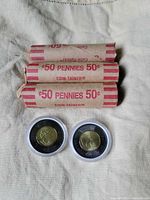 Three rolls of Canadian pennies and two 2022 black toonie coins in protective cases shown on cloth background.