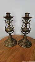 Front view of two ornate cast metal freestanding gimbal candlestick holders on a wooden table