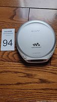 Top view of the silver Sony Walkman portable CD player placed on a wooden surface alongside a lot number card