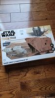 Full view of sealed Star Wars paper model kit box showing images of Razor Crest and Sandcrawler models, branding, and piece count.