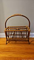 Front view of vintage boho style rattan magazine rack showing woven vertical slats and arched handle.