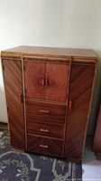 Front view of vintage wooden wardrobe showing marquetry inlay on doors and drawers with reddish Bakelite handles.