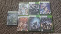 Eight Xbox 360 game discs arranged on floor showing cover art including Halo 3, Halo Reach, Halo Wars, Tekken 6, Soulcalibur IV, and Tales of Vesperia