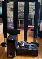 Four tall LG tower speakers with mesh fronts and silver base accents, LG subwoofer, small speaker, Yamaha receiver, remote control, and speaker wire on wooden floor in front of stone fireplace.