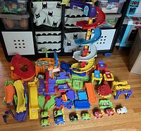 Overview of entire VTech race track toy set, showing multiple parts, ramps, and toy vehicles spread on floor