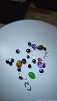 Mixed polished natural gemstones under spotlight showing various colors and shapes including purple amethyst, black and white snowflake obsidian, golden tiger's eye, clear quartz, and red garnet