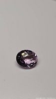 Oval purple Brazilian amethyst gemstone with checkerboard cut lying on a white background, showing high luster and clarity.