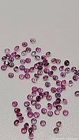 Top down view of scattered tiny pink sapphires showing round shapes and variation in light reflection.