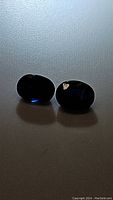 Pair of deep blue oval cut sapphires on a textured light background, showing rich dark blue color and oval shape.