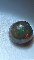 Close-up photo of a round free form Ethiopian black opal cabochon showing vibrant red and green play of color on its surface.