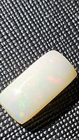 Close-up photo of the natural Ethiopian opal rectangular cabochon showing play of color on a dark textured background.