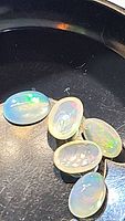 Five oval cabochon natural Ethiopian opals with play-of-color on a black background, showing translucency and flashes of color.