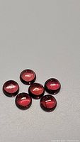 Six round cabochon garnet gemstones laid out on a gray background, showing their size and glossy surface.