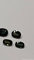 Four oval green sapphires with blue undertones, shown on a white background, with faceted oval cuts and good clarity.