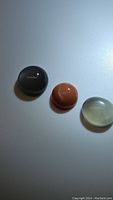 Photo showing three polished moonstone cabochons of different colors (dark gray, orange, light translucent) on a white background.