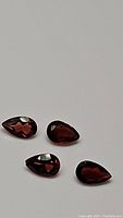 Four pear cut garnet gemstones photographed from above with a grey background showing their deep reddish-brown color and faceting.