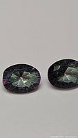 Close-up photo of two oval cut Mystic Topaz gemstones showing their faceted surfaces and color reflections.