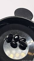 Five polished oval black onyx cabochon gemstones on a reflective surface. Stones appear to be about similar size, one with white veining visibility.