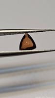 Close-up photo of the triangular deep orange Cambodian zircon gemstone held by tweezers, showing its color and clarity.