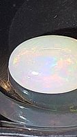 Close-up image showing oval cabochon cut opal with visible play-of-color on milky white base.