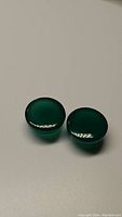 Pair of round cabochon green onyx gemstones on a neutral background with visible light reflection.