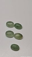 Five oval mint green kyanite cabochons with visible inclusions on a white background.