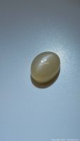 Oval cabochon peach moonstone gemstone showing smooth polished dome and translucent peach color under light.
