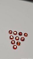 Top view of 10 round faceted imperial sapphires with deep orange color on white background.
