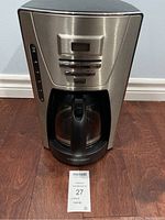 Front view of the Black & Decker coffee maker on a hardwood floor, showing the glass carafe and body.