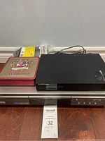 Full lot showing Samsung players, power cord and tin box on wood floor.