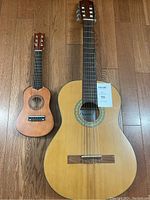 Photo showing classical guitar and smaller guitar side by side on wood floor