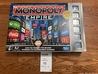 Box front showing Monopoly Empire branding and Times Square themed artwork with brand logos.