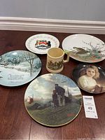 Photo showing four decorative plates and one ceramic cup on wooden floor, highlighting designs and overall condition.