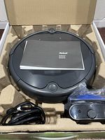 Top view of iRobot Roomba 694 vacuum with user manual placed on top, inside packaging.