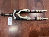 Full view of used white RockShox USA mountain bike front suspension fork with decals and rubber boots, lying on hardwood floor.