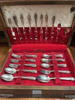 Full view of the open wooden silverware box displaying the knives, forks, and spoons neatly arranged in red velvet slots with a cream quilted interior lid.