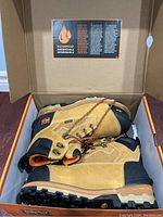 Pair of tan and black Timberland PRO steel toe boots inside the open box showing waterproof label on lid.