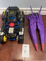 Black Batmobile and purple starship toy vehicles side by side on floor